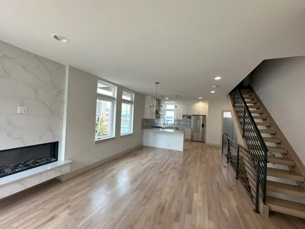 A living room with hardwood floors , a fireplace , stairs and a kitchen.